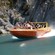 Guests wearing life jackets riding a jet boat at high speed near rocky cliffs